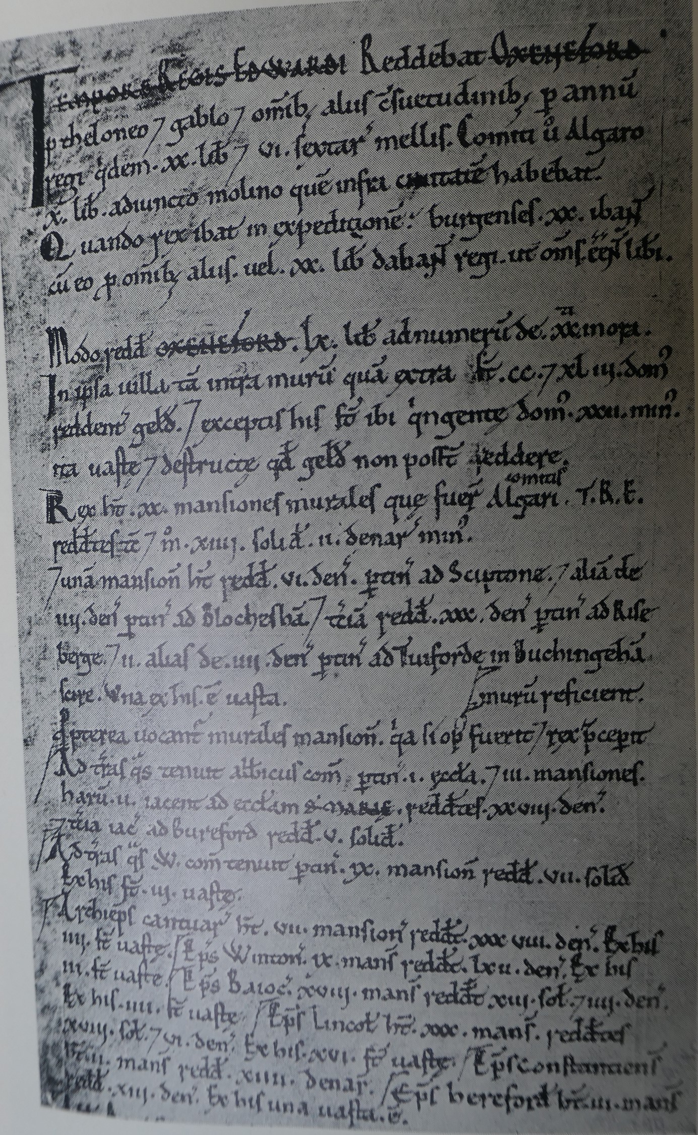 A single page of the Domesday Book manuscript: one tall column of dense medieval Latin in dark ink on parchment, with several headings and place-names picked out in red, shown in black-and-white.